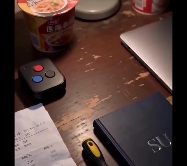 桌上放着带红蓝黑三色按钮的控制器与印有SU字样的笔记本