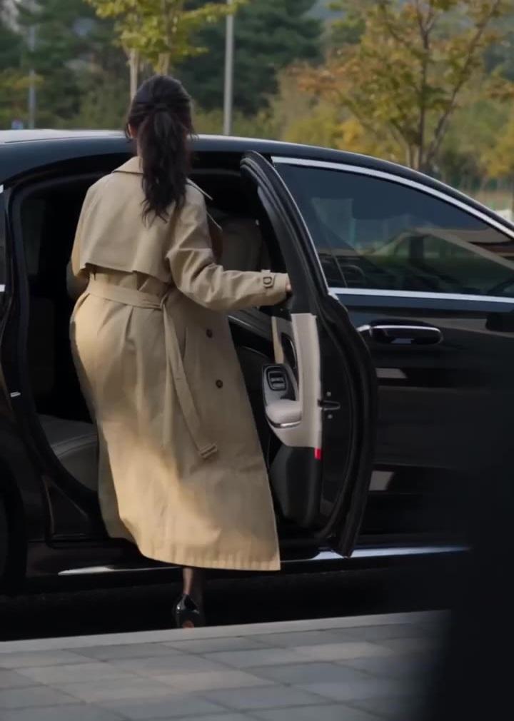 女主披浅色风衣走向停靠的车辆